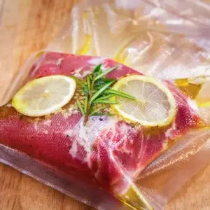 Das Foto zeigt ein Stück mariniertes Fleisch mit Gewürzen in einem Vakuumbeutel einvakuumiert.
