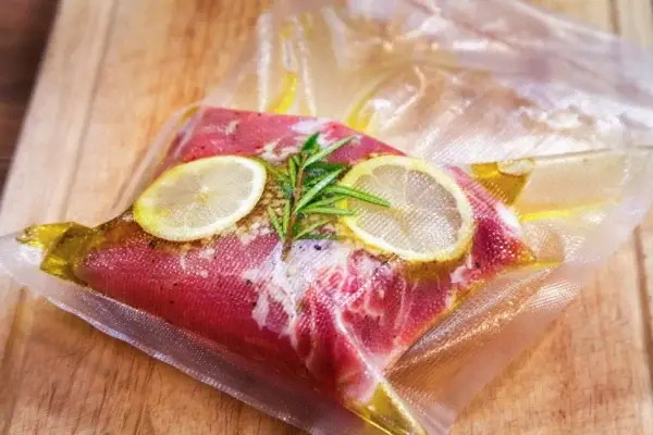 Das Foto zeigt ein Stück mariniertes Fleisch mit Gewürzen in einem Vakuumbeutel einvakuumiert.