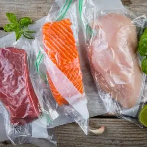 Auf dem Bild sieht man verschiedene Fleisch und Fischsorten in Vakuumbeuteln auf einer Holzoberfläche liegend.