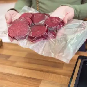 Ein strukturierter Vakuumbeutel mit einigen vakuumierten rote Beete Scheiben in den Händen einer Frau.